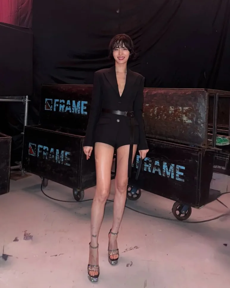 Nana posing behind the scenes in a black belted romper and high heels
