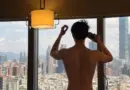 Park Bo-gum standing with his back to the camera beside a window overlooking the city