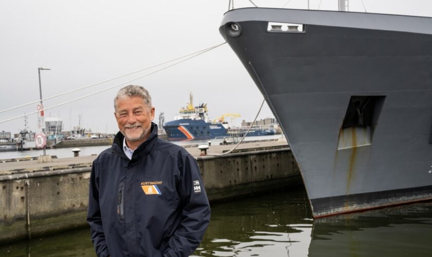 Jan van Zanten poseert in haven met een Marine- en Kustwachtschip op de achtergrond.