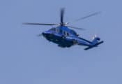 De blauwe politiehelikopter AW139 vliegt door een strak, blauwe lucht.