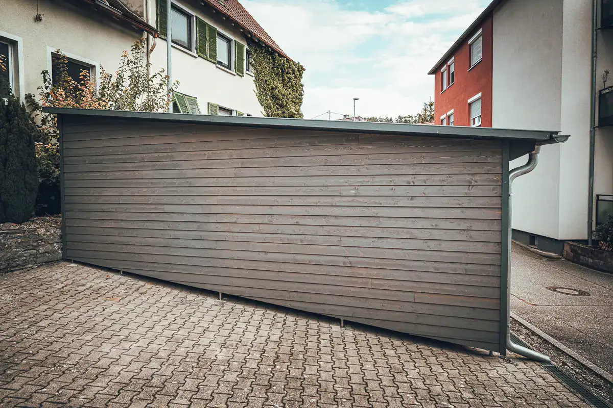 Lauffers klassisches Bauprojekt: moderner Carport in Holzverschalung mit Stützfüßen für den konstruktiven Holzschutz.