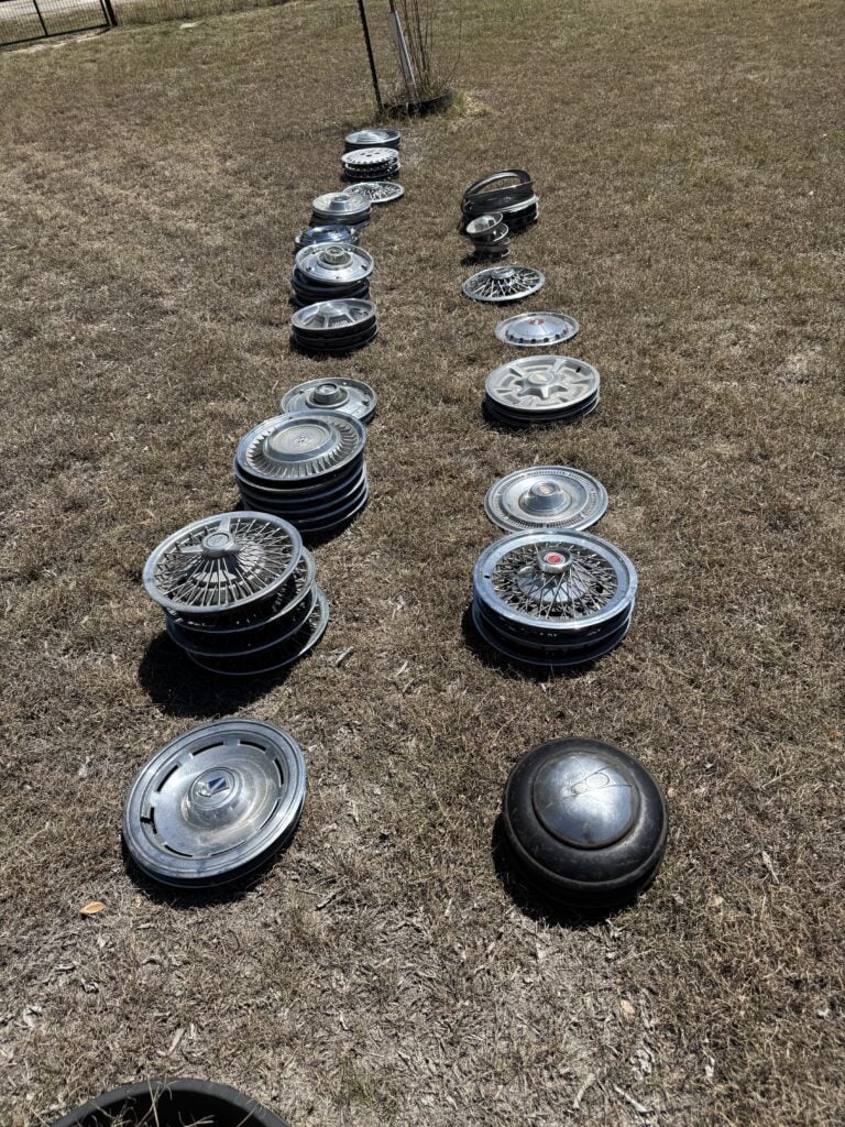 Vintage car hubcaps and wheel covers arranged on grass at an estate auction.
