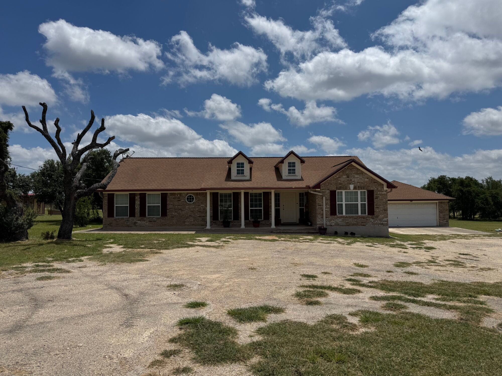 Spacious ranch-style house with front porch and garage under a blue sky.