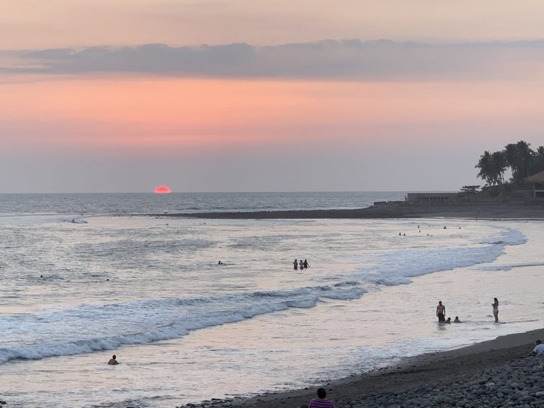 Sunset over the ocean with people relaxing on the sandy shore.