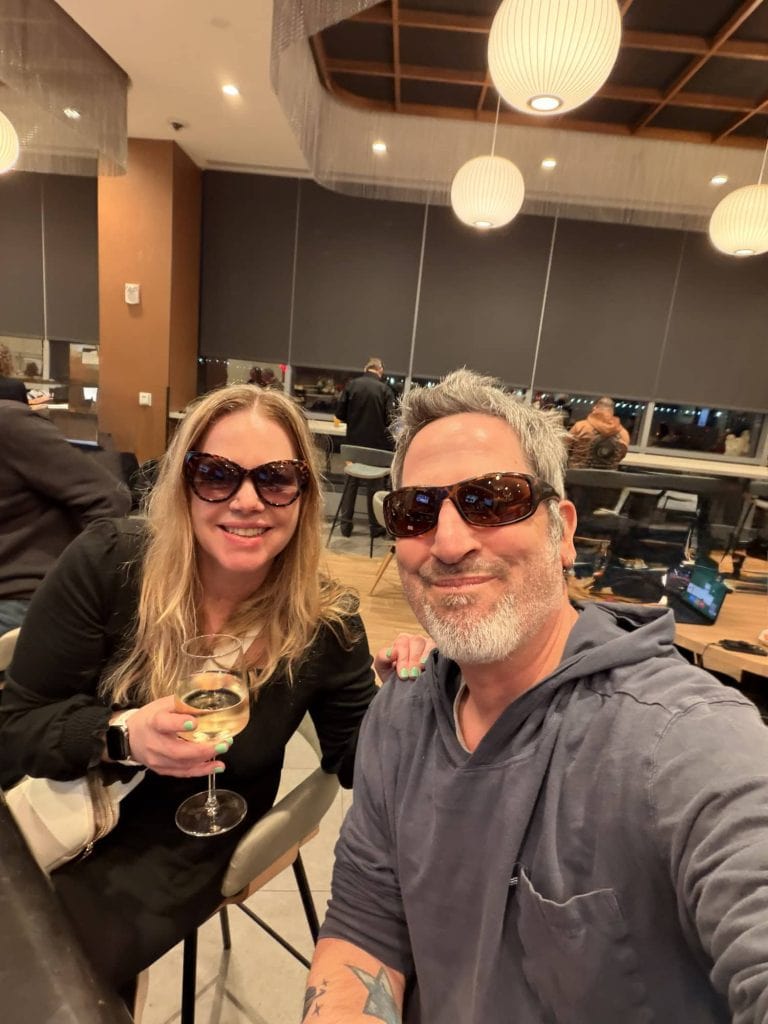 Travel couple enjoying dinner at a modern restaurant with city views in the background.