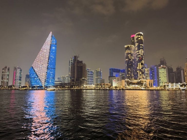 Night cityscape of modern skyscrapers with colorful lights along the waterfront.