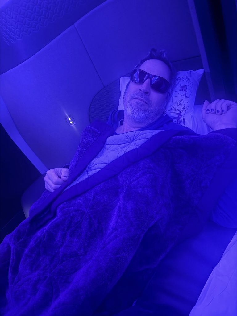 Man relaxing in bed with sunglasses, cozy blanket, and modern decor.