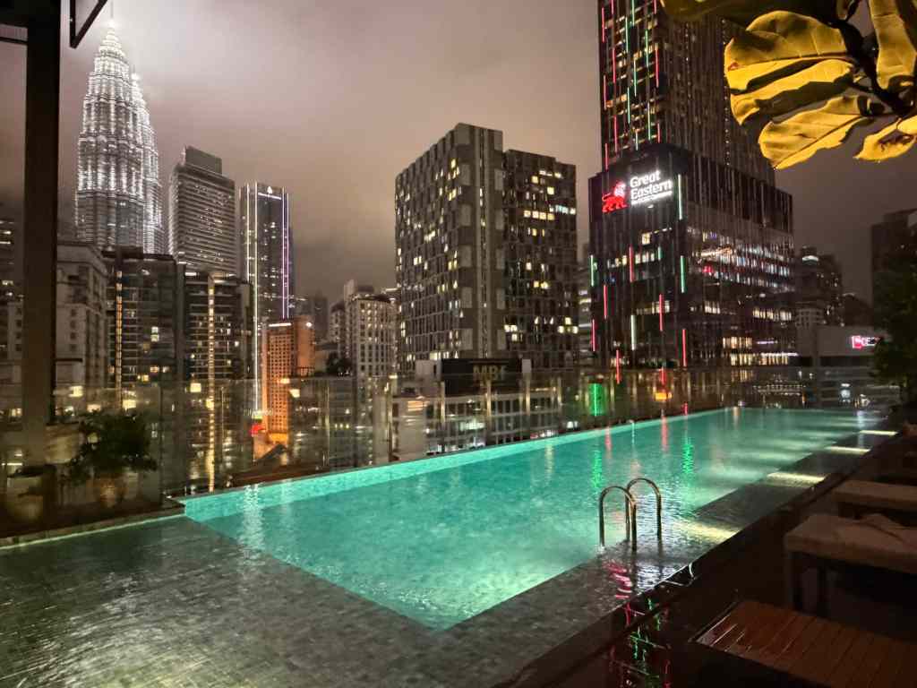 Rooftop pool overlooking Kuala Lumpur's iconic skyline with Petronas Towers at sunset.