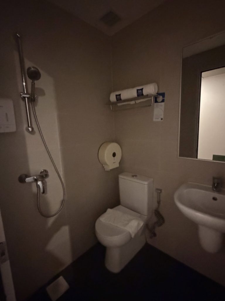 Small hotel bathroom with shower, toilet, and sink in a modern setting.