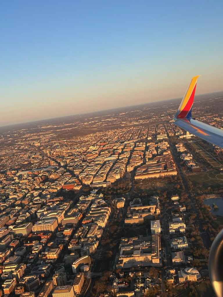 Aerial view of a city with buildings and streets from an airplane window during sunset.