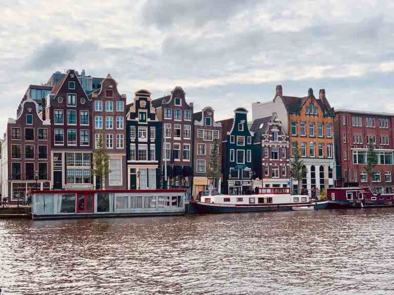 Colorful canal houses in Amsterdam with boats on the water.