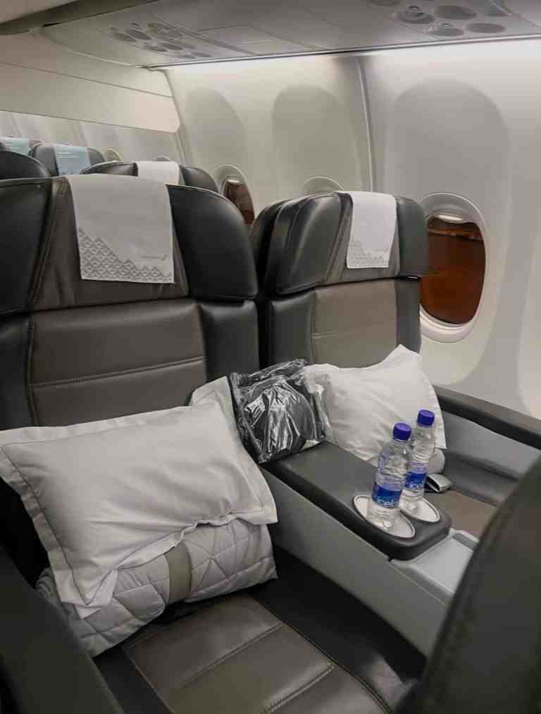 Business class airplane seat with pillows and water bottles on tray table.