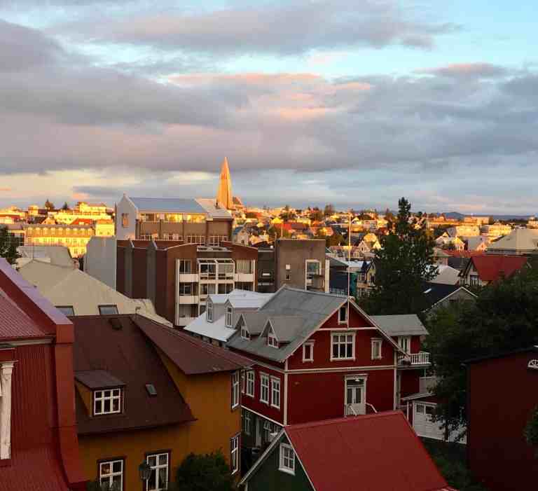 Vibrant rooftops and city skyline with a church spire during sunset.