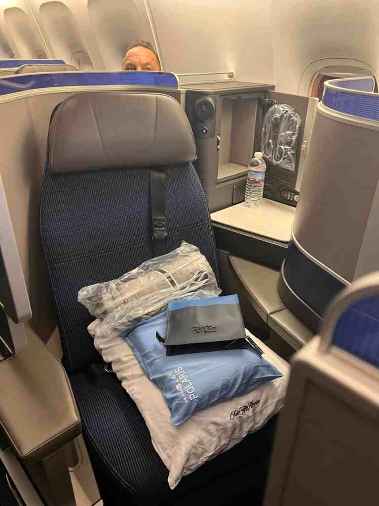 Airplane seat with travel essentials including water bottle, headphones, and travel pillow.