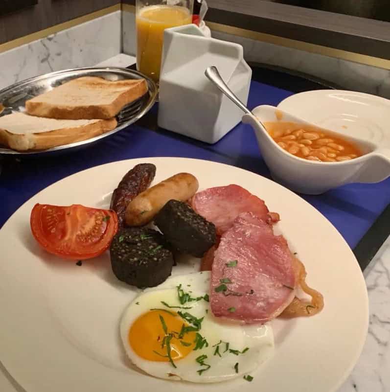 Breakfast plate with eggs, sausages, bacon, and tomato for a hearty morning meal.