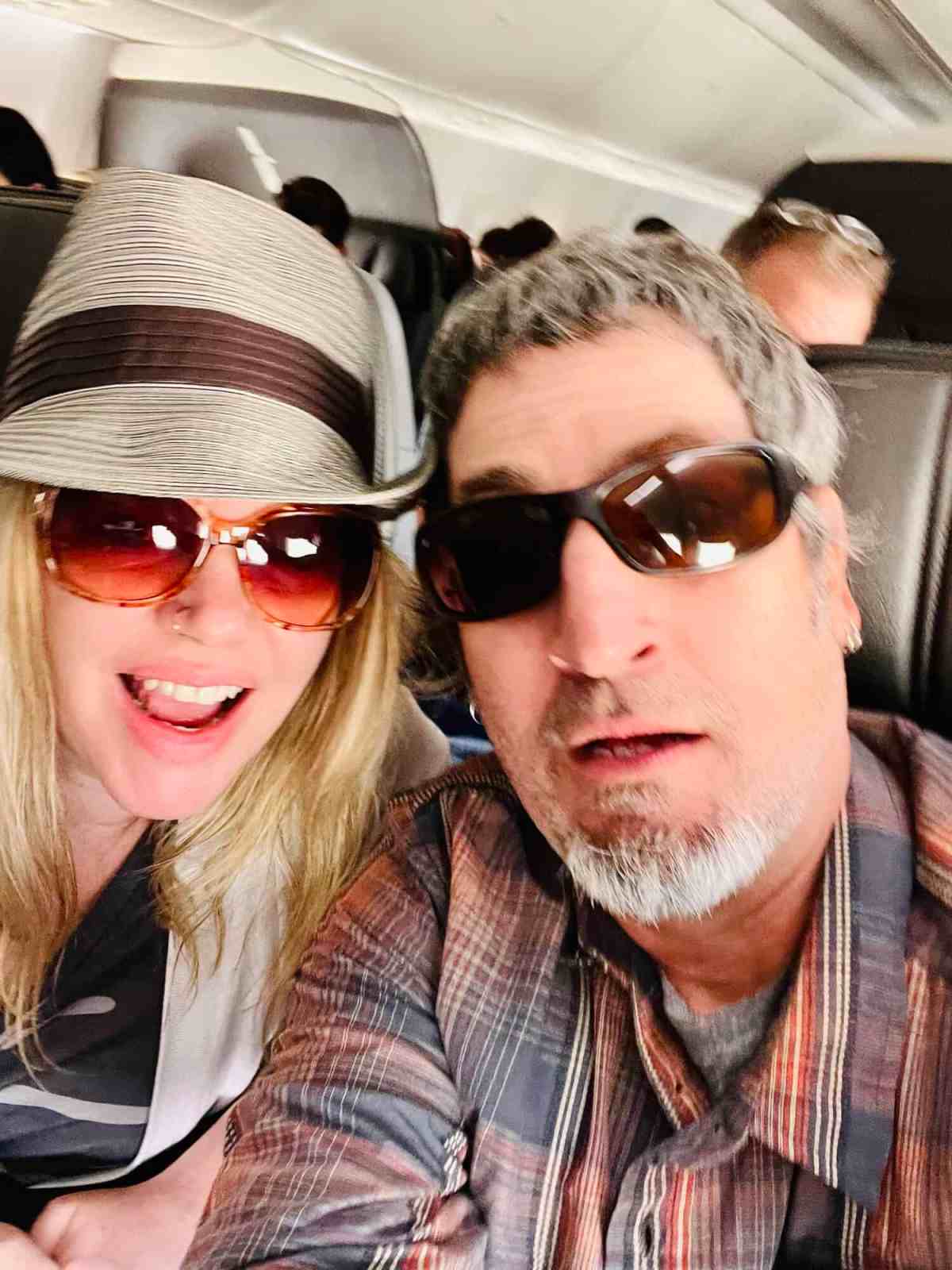 LiAnn and Theo wearing sunglasses on airplane, smiling for selfie.