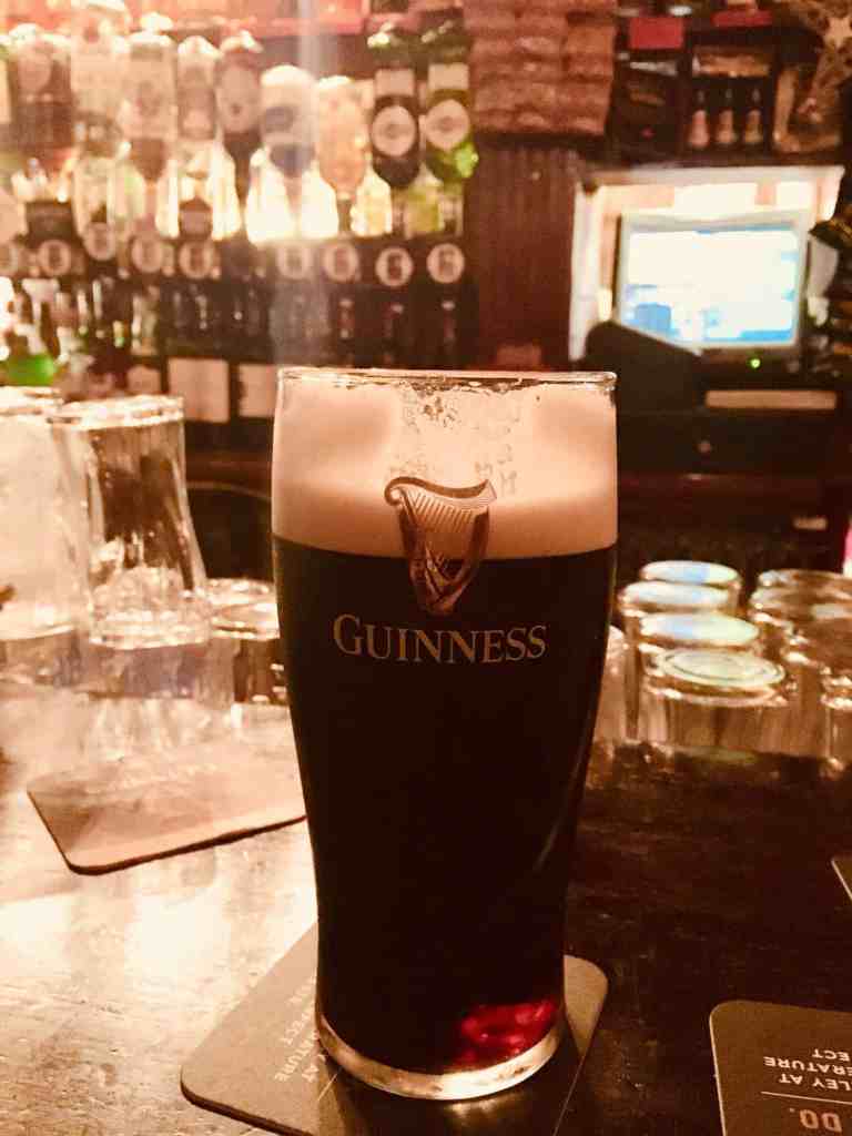 A pint of Guinness beer on a bar counter in a pub setting.