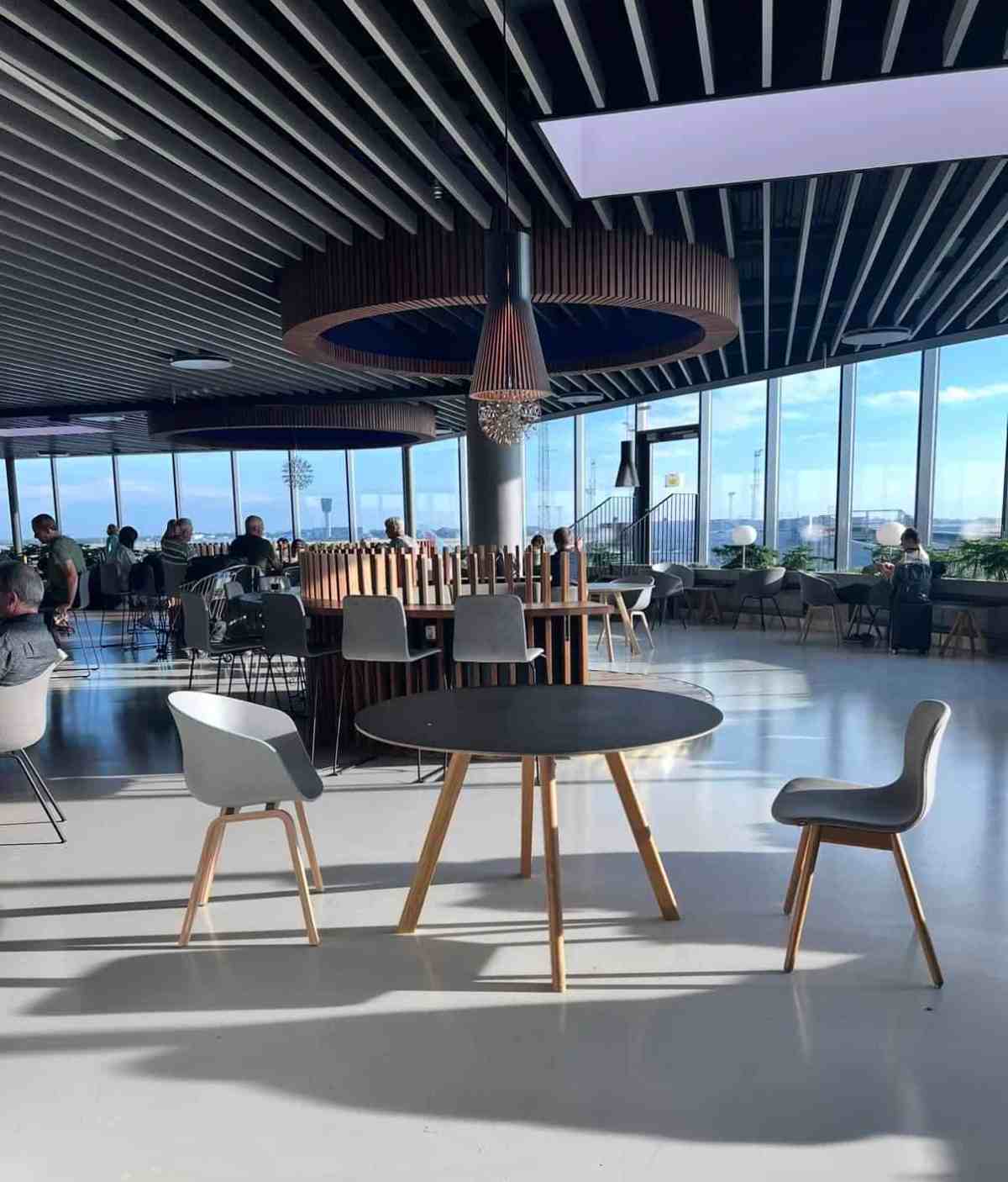 Modern airport lounge with seating and panoramic city view.