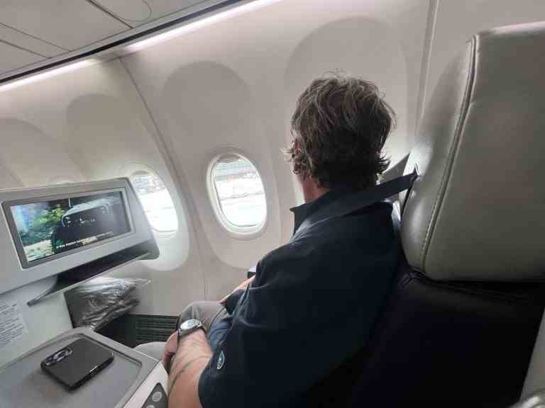 Passenger looking out airplane window during flight with personal device nearby.