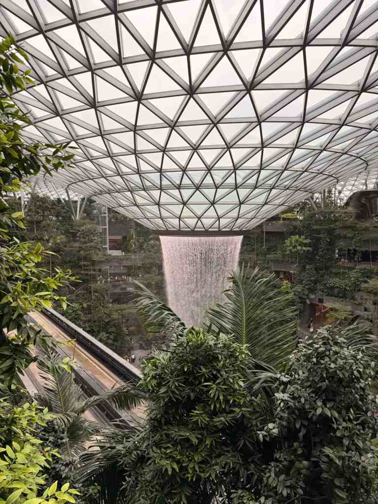 Indoor garden with waterfall and lush greenery under a glass dome.