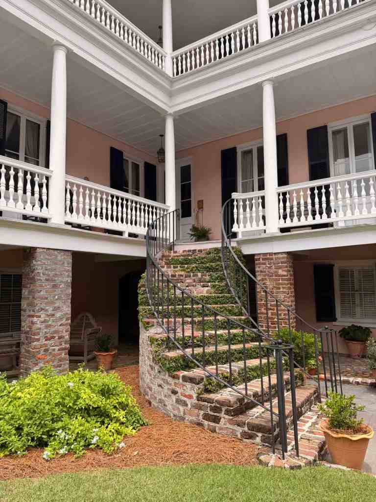 Elegant historic mansion with brick and white porch, spiral staircase, and lush garden.