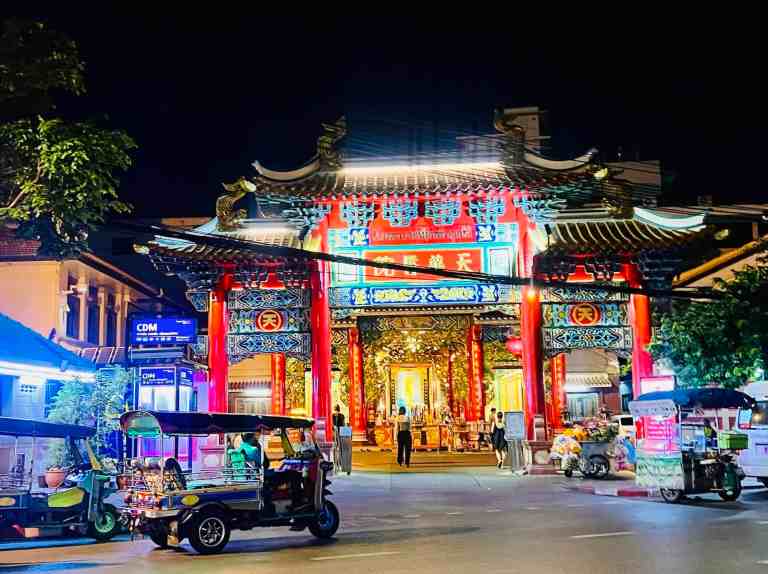 Colorful Chinese temple illuminated at night with street vendors nearby.