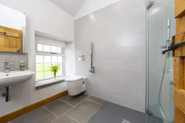 Rustic-style accessible wet room with wall-mounted toilet basin, foldable shower screen, hand rail, and large easy-press buttons for enhanced accessibility. Life Quality Bathing.