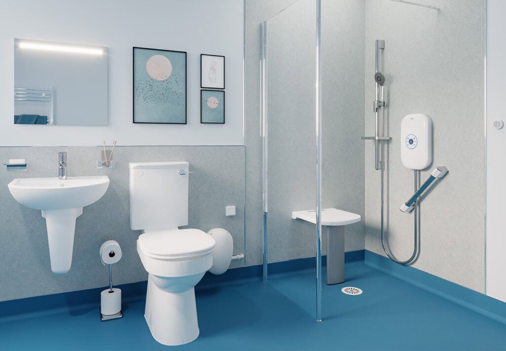 Wet room with bright deep blue anti-slip flooring. Shower with fold down seat ad grab rails. Glass screen in-inbetween shower and toilet. tea themed picture frames and mirror above white sink