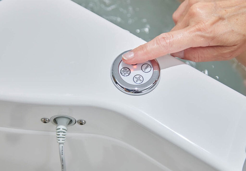 finger pressing 1 of 4 buttons in circular chrome-look material, used to control setting of bath.