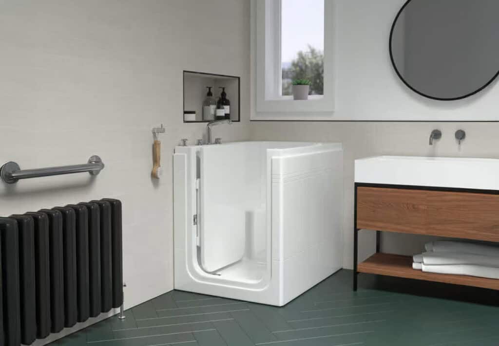 Compact walk in bath the Taranto (Maestro). Large door opening. Simplistic mobility bathroom. Long black radiator on wall, dark wooden cabinet with white sink on top. Tall but thin window. behind bath.