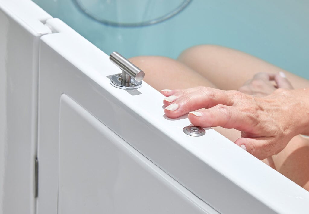 Hand from person bathing pressing metal button on top of the bath next to the side door