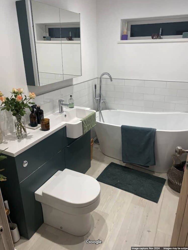 Mr Roddick's new bathroom. White oval bath, sink and toilet. Dark green colour theme with matching towels and furniture. White walls and half height white tile-effect wall boards