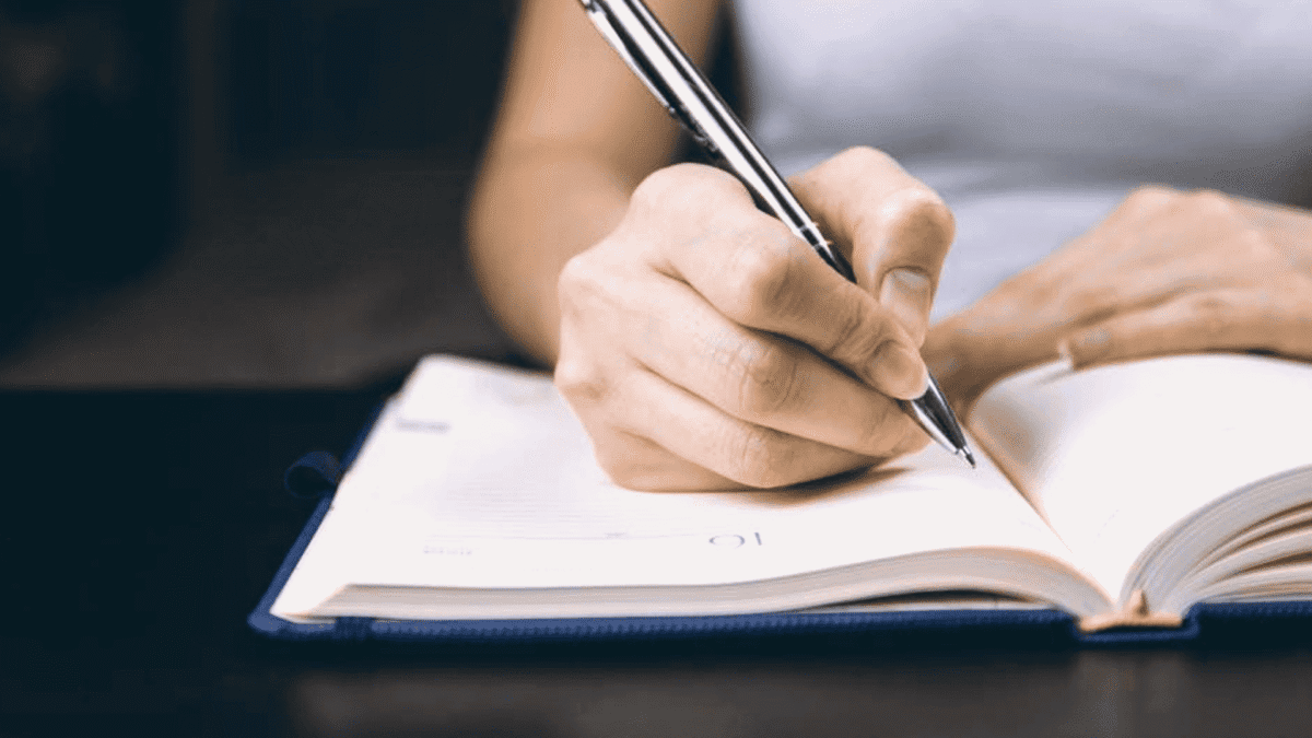 Why ISBN is Important for Self-publishing A hand, gripped by literary ambition, scribbles on an open notebook atop a dark desk; the rest of reality politely blurs away.