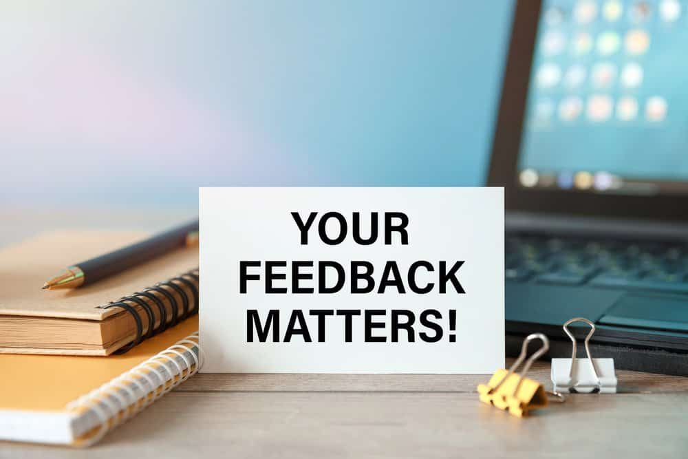 A white card shouts YOUR FEEDBACK MATTERS! atop a jumble&mdash;spirals, pen, clips, and a laptop lurking like a shy wizard.