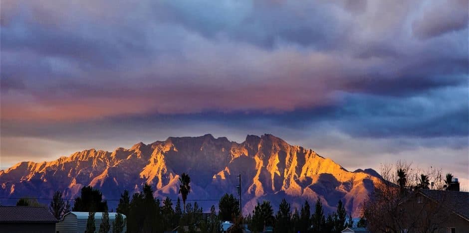 Golden-lit mountain range at sunset with residential homes in the foreground.