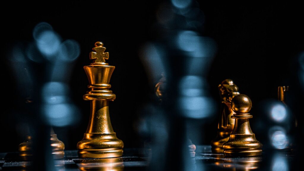 A close-up of a chess game with gold and black pieces on a dark background.