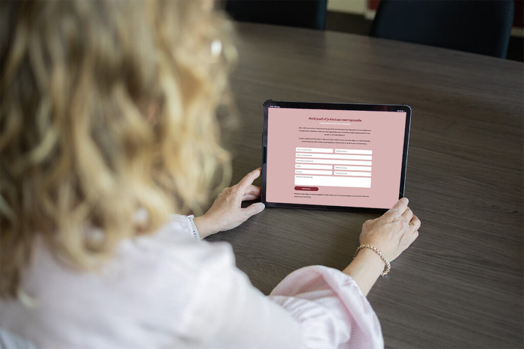 Vrouw houdt tablet vast met aanmeldformulier voor logopedie bij de Lindevallei op het scherm