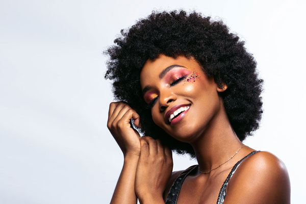 Afro chic avec maquillage coloré et brillant, souriante et confiante.