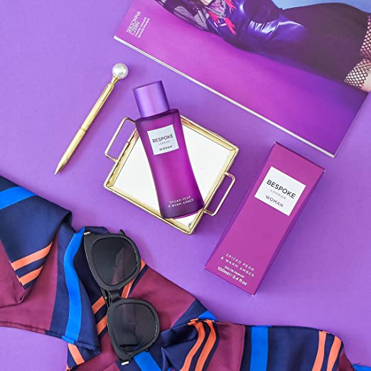 Bouteille de parfum BESPOKE pour femme avec accessoires de mode et produits de beauté, sur fond violet.