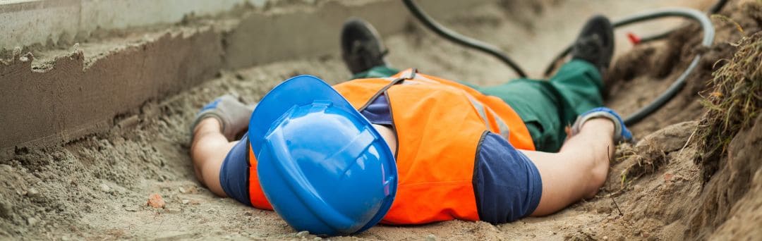 Worker lying on ground with safety helmet in trench, emphasizing lone worker safety devices.