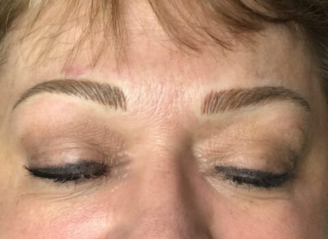 Close-up of a woman's face with neatly arched eyebrows, neutral eyeshadow, and black winged eyeliner with eyes closed.