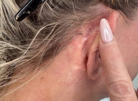 Close-up of a person touching their ear with a pink glittery nail, a black hair clip in the hair nearby.