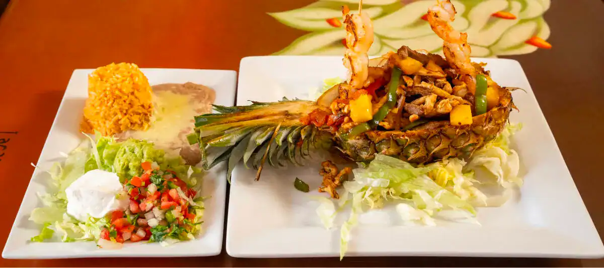 Tasty pineapple tacos with shredded meat and fresh vegetables on a white plate.