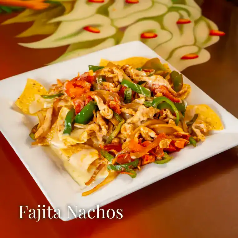 Tasty fajita nachos with peppers, chicken, and cheese on a white plate.