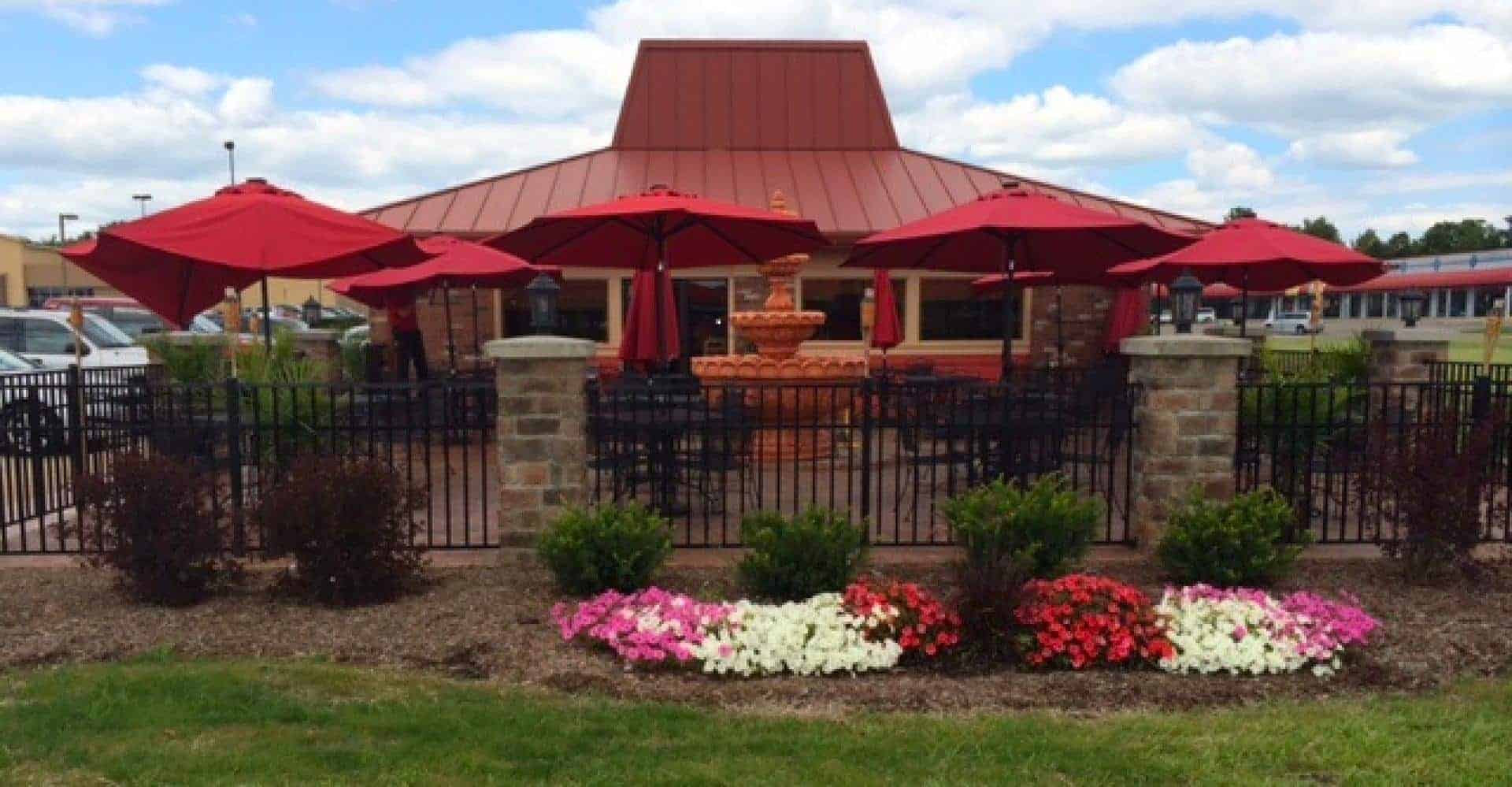 Outdoor restaurant seating with red umbrellas and lush landscaping.