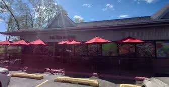 Exterior view of a restaurant with red umbrellas and a traditional roof.