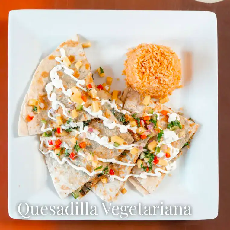 Vegetarian quesadilla topped with colorful vegetables and creamy sauce, served with a crispy rice ba.