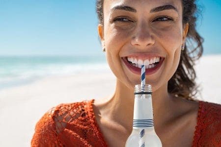 Bright smiling woman drinking soda at the beach, showcasing dental health.
