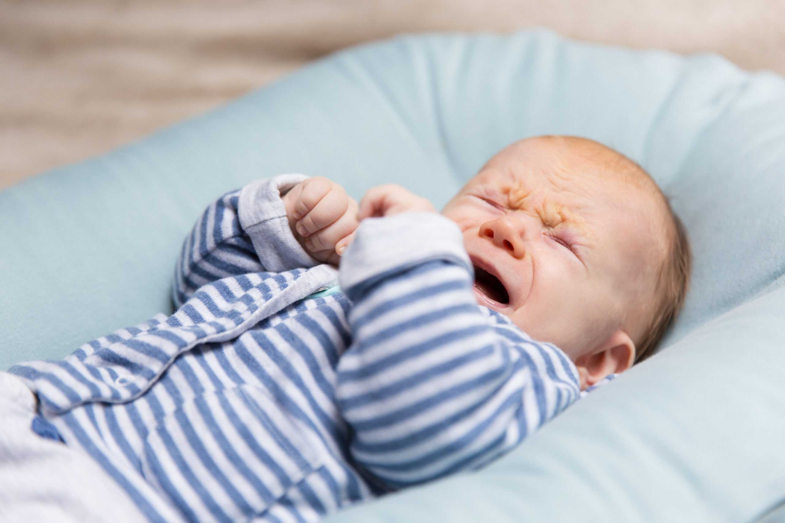 Screaming baby with teething discomfort on a pillow.