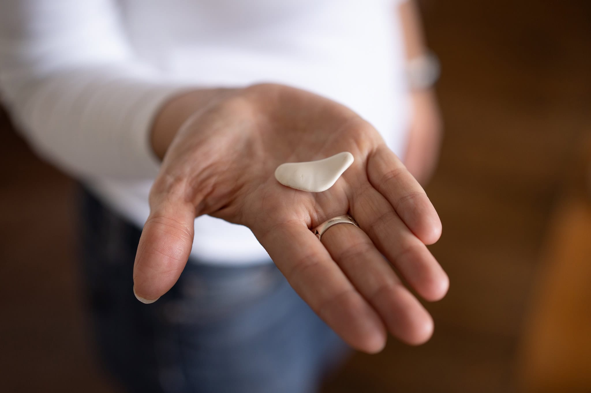 Fiona Buckland's hand holds a small white object, with soft light illuminating her skin.